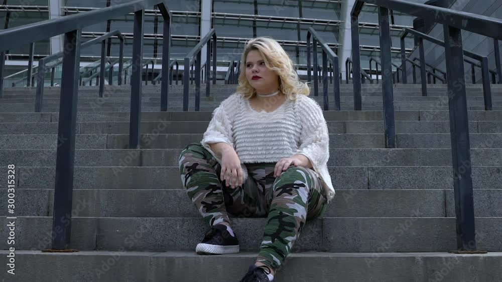 Beautiful plus size girl confidently looking around, sitting on urban stairs Beautiful plus size girl confidently looking around, sitting on urban stairs