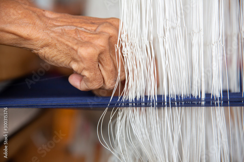 Cotton weaving. Close-up woman hand weaving cotton on manual loom. Thai cotton handmade. Homespun fabric process. The process of fabric weaving in vintage weaver machine. Selective focus.