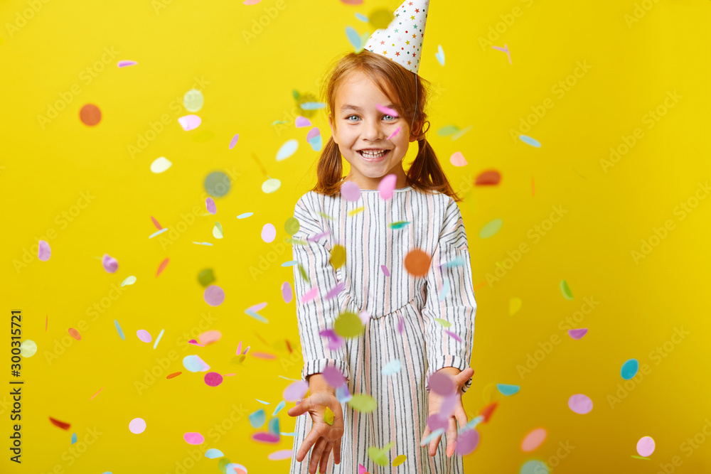 Studio portrait of happy birthday child girl with confetti on colored background.