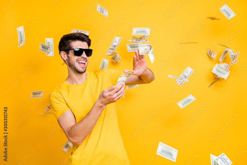 Photo of young handsome careless guy throwing usa money banknotes away wealthy person wear sun specs casual t-shirt isolated bright yellow color background - obrazy, fototapety, plakaty 