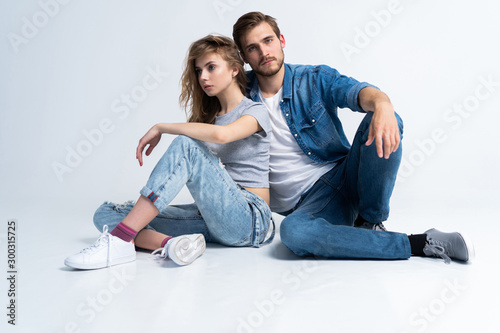 Portrait Of Happy Young Couple Sitting On Floor Leaning Against Wall