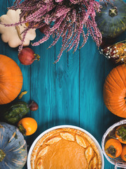 Autumn thanksgiving moody background with pumpkin pie, different pumpkins, fall fruit and flowers on green rustic wooden table. Flat lay