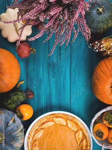 Autumn thanksgiving moody background with pumpkin pie, different pumpkins, fall fruit and flowers on green rustic wooden table. Flat lay