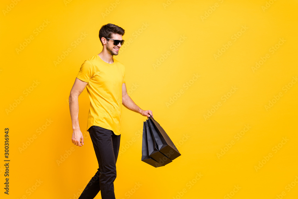 Photo of handsome guy holding boutique bags making abroad shopping going down fashionable mall floor wear casual t-shirt pants isolated yellow color background Photo of handsome guy holding boutique bags making abroad shopping going down fashionable mall floor wear casual t-shirt pants isolated yellow color background