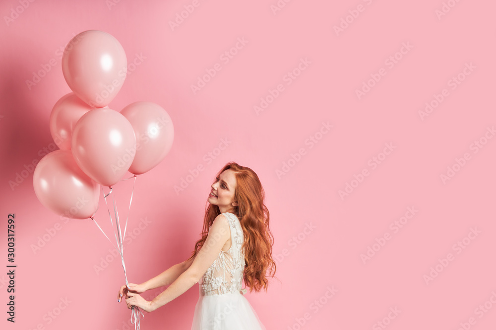 Portrait of caucasian appearance stand wearing wedding dress with pink air balloons. Happy