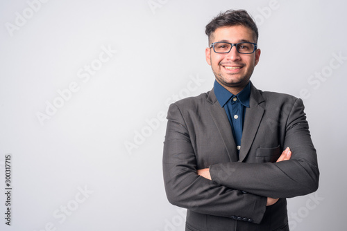 Portrait of happy young Persian businessman in suit smiling with arms crossed