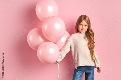 Portrait of caucasian kid girl with pink air balloons, long hair and big beautiful eyes, wearing white blouse and jeans.