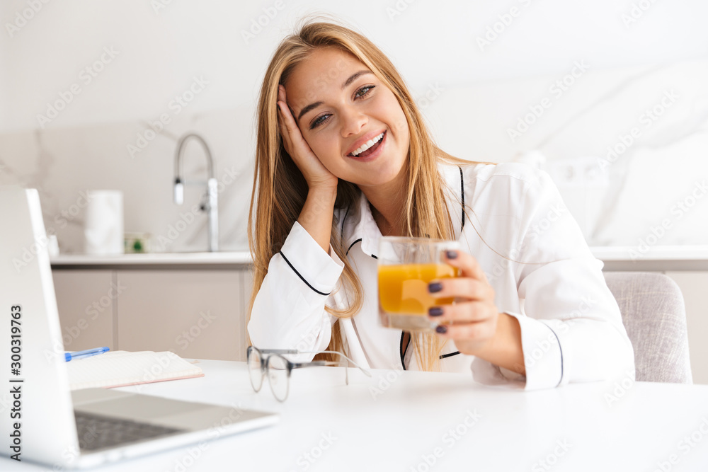 Photo of smiling blonde woman working with laptop and drinking juice Photo of smiling blonde woman working with laptop and drinking juice