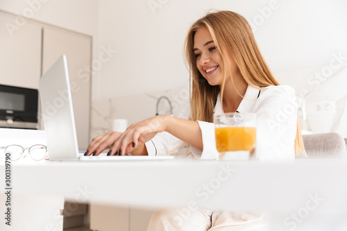 Photo of smiling cute woman working with laptop and drinking juice