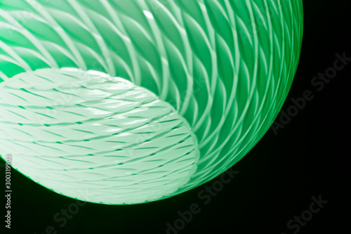 Toned photo of luminous lampshade in darkness. Close-up of lighting fixture. Abstract architecture detail. Glowing object with ripple pattern in concept of home interior and green technologies.