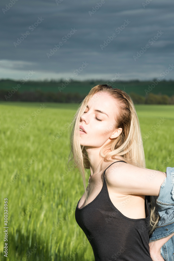 Beautiful blonde girl is standing in a field against a background of clouds. Beautiful blonde girl is standing in a field against a background of clouds.