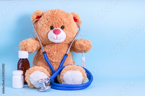 Teddy bear, stethoscope, thermometer, pills and cough syrup on blue background with space to copy; fun Pediatrics concept; children's medicine