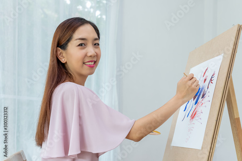 Woman female artist painting picture at home as her hobby, looking at camera