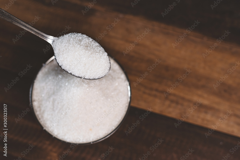 Sugar poured into a steel bowl on a wooden table. Concept of unhealthy eating and diabetes Sugar poured into a steel bowl on a wooden table. Concept of unhealthy eating and diabetes