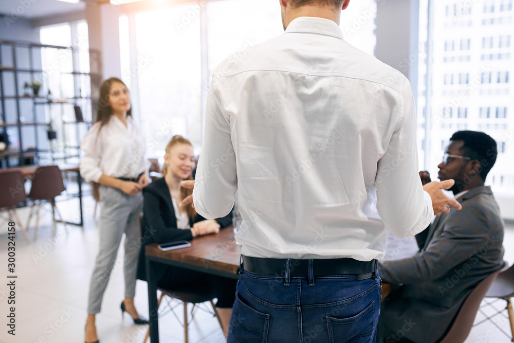 View on back of man in white shirt speaking with international group of business people View on back of man in white shirt speaking with international group of business people