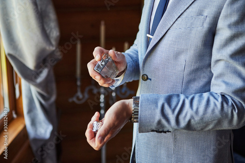 Handsome guy is choosing perfumes, Elegant man in suit using cologne,groom getting ready in the morning before wedding ceremony. Men Fashion