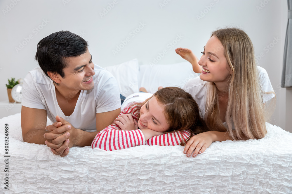 Happy family, including father mother and daughter, are lying down on bed with smile, looking at each other