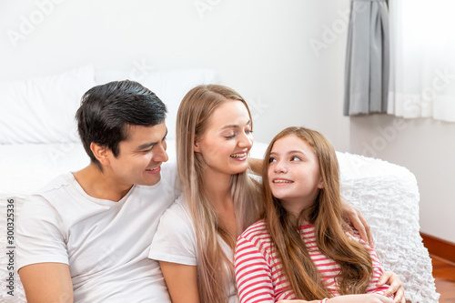 Happy family, including father mother and daughter, are sitting in front of bed with smile, looking at each other