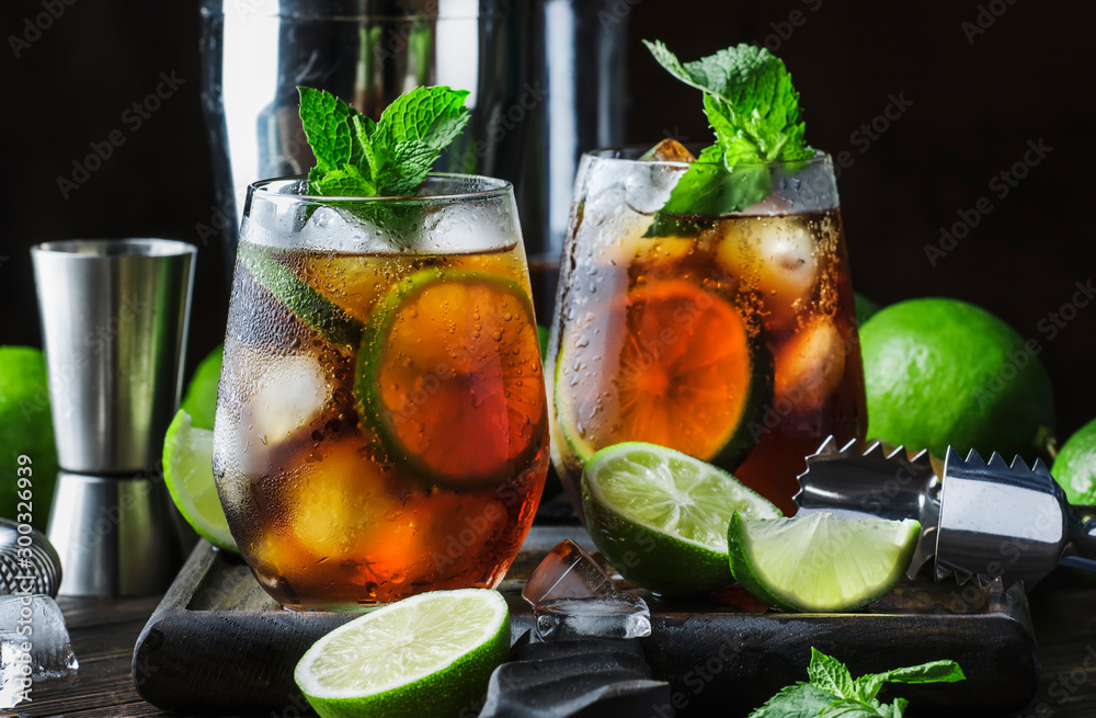 Cuba libre alcohol cocktail with golden rum, lemon juice, cola, lime and ice, dark bar counter background, bar tools, place for text - obrazy, fototapety, plakaty 