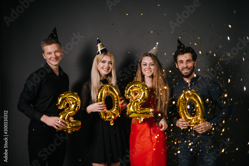 Cheerful young friends holding inflatable foil numerals 2020. Shooting in professional studio on isolated black background.