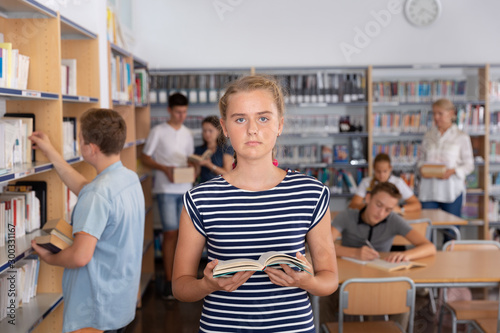 Schoolgirl standing with book before lesson in school library