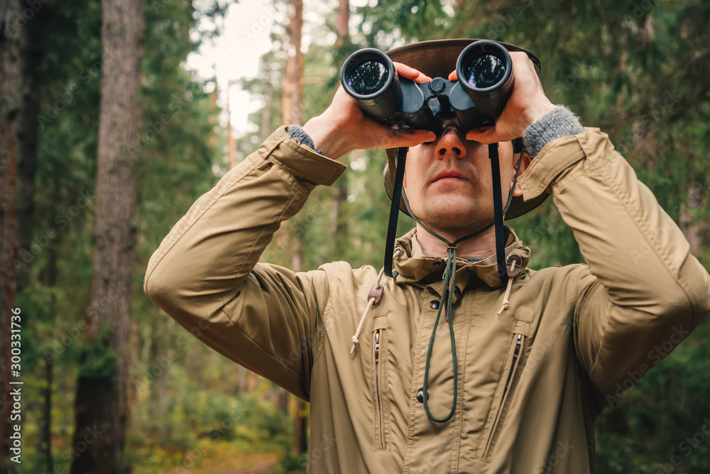 A man in a hat and uniform green and beige holds binoculars and looks into the distance, Ranger watching the territory, the protection of the reserve A man in a hat and uniform green and beige holds binoculars and looks into the distance, Ranger watching the territory, the protection of the reserve