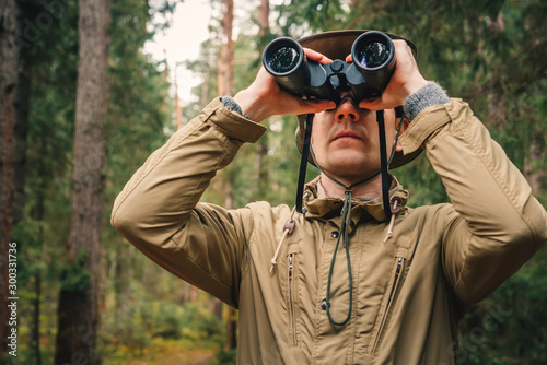 A man in a hat and uniform green and beige holds binoculars and looks into the distance, Ranger watching the territory, the protection of the reserve