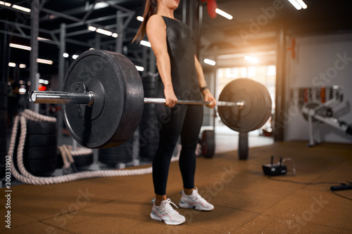 Young unrecognizable woman with heavy barbell in hands, doing squats, preparing for powerlifting competition, spending time in modern gym, active people concept, side sho