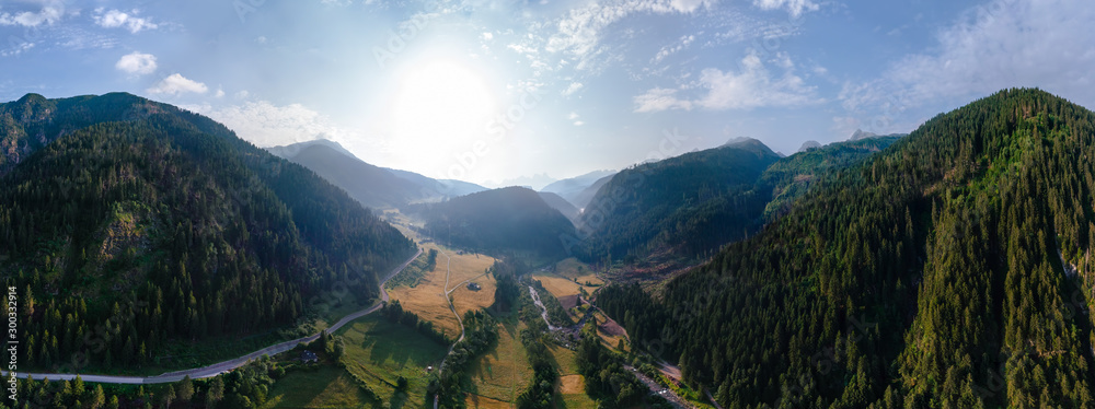 Fototapeta premium Wide aerial view of a camping site, recreation with a tent and parking for a motor home, camper van, sunrise summer, mountains and a river near the town of Predazzo, Trentino, Italy, Europe