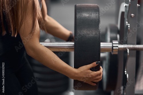 Close view of gentle female hands preparing heavy barbell for training in modern fitness studio, side indoor shot