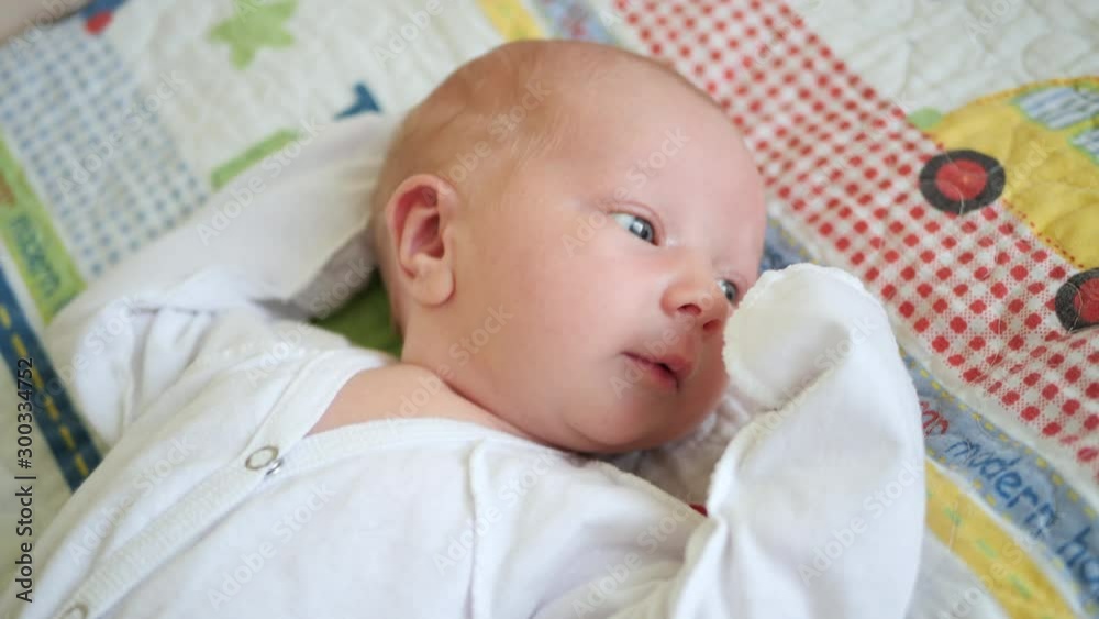 Portrait. Close-up. The baby in white clothes lies on his back and puts his hand in his mouth. Portrait. Close-up. The baby in white clothes lies on his back and puts his hand in his mouth.