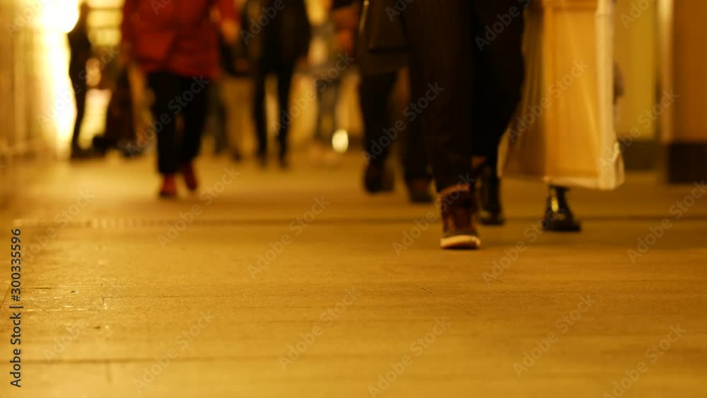 People walk in the underpass. Metro station. Silhouettes of unrecognizable people passing by blurred. Artificial lighting with orange lamps on the walls. Focus and closeup on shoes.