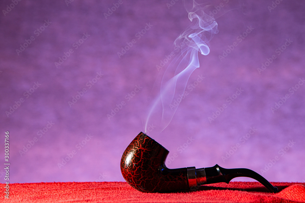 Dark red smoking pipe and dancing smoke with purple background on red carpet stock photo