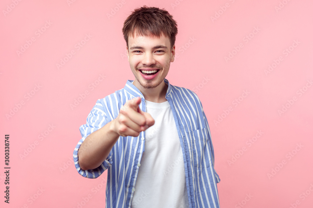 Hey you! Portrait of young joyous brown-haired man with small beard and mustache in casual shirt pointing at camera and laughing, making fun towards you. indoor studio shot isolated on pink background Hey you! Portrait of young joyous brown-haired man with small beard and mustache in casual shirt pointing at camera and laughing, making fun towards you. indoor studio shot isolated on pink background
