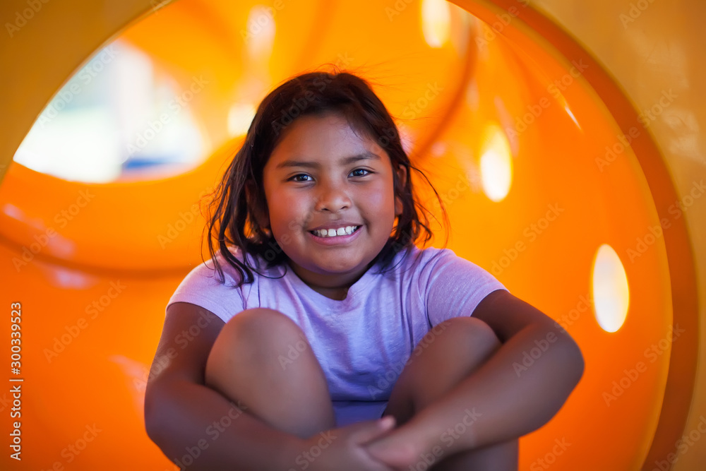 A nine year old girl having fun playing in a yellow playground slide. - obrazy, fototapety, plakaty 