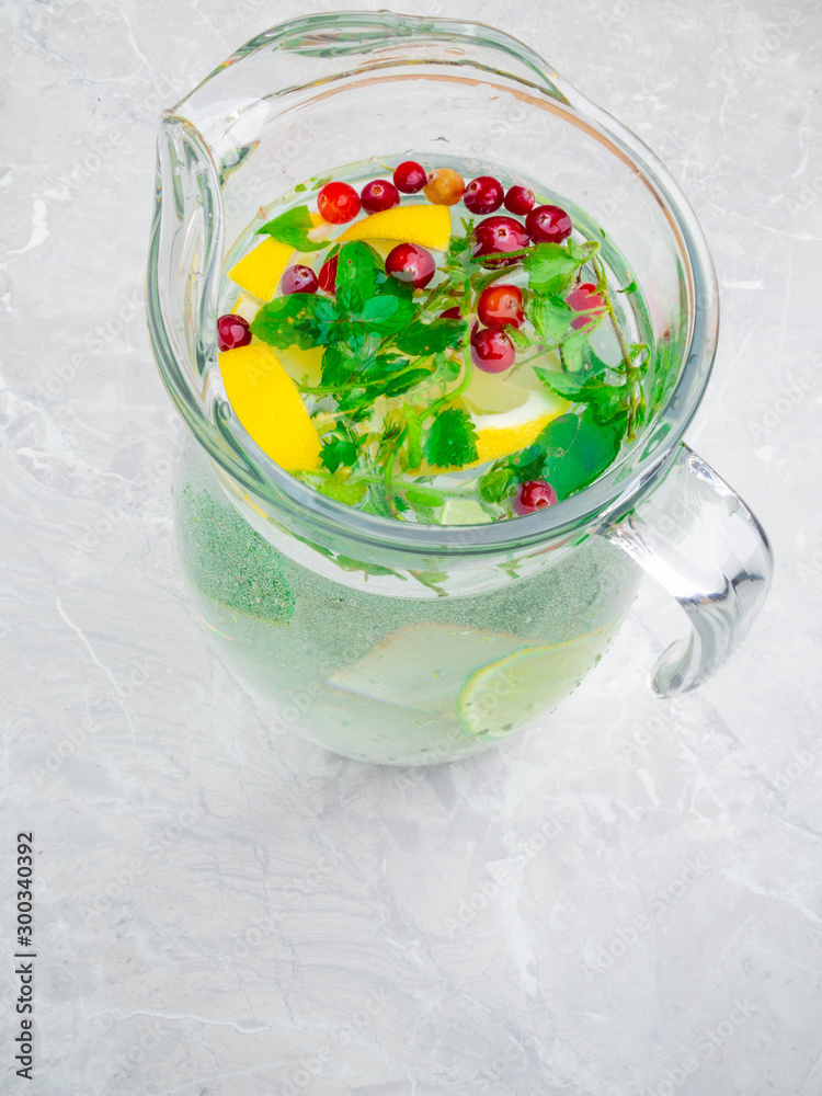 Homemade lemonade with fresh lemon and lime slices, mint leaves, red berries in pitcher on the table Homemade lemonade with fresh lemon and lime slices, mint leaves, red berries in pitcher on the table