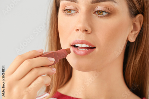 Beautiful young woman with lipstick on light background