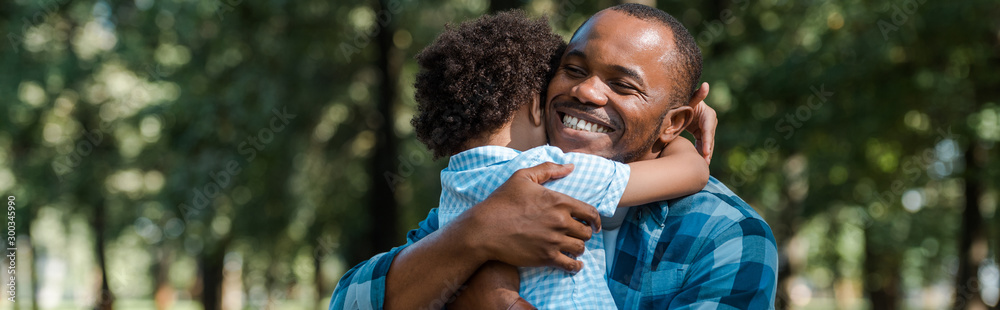 panoramic shot of happy african american father hugging son - obrazy, fototapety, plakaty 