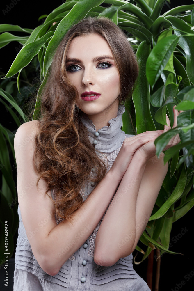 Fototapeta premium Portrait of a beautiful brunette girl in a white shirt with a green flower in studio