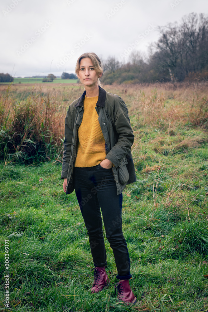 Portrait of a blonde woman standing in field with hand in her pocket