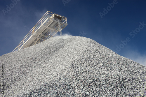 Conveyor line transporting crushed ore and pile of gravel against the blue sky, close-up. Mining industry. Mine and quarry equipment.