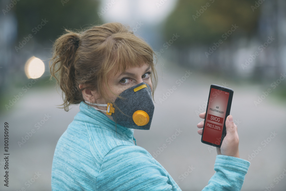 Plakat Kobieta nosząca prawdziwą maskę antysmogową i sprawdzająca aktualne zanieczyszczenie powietrza za pomocą aplikacji na smartfona