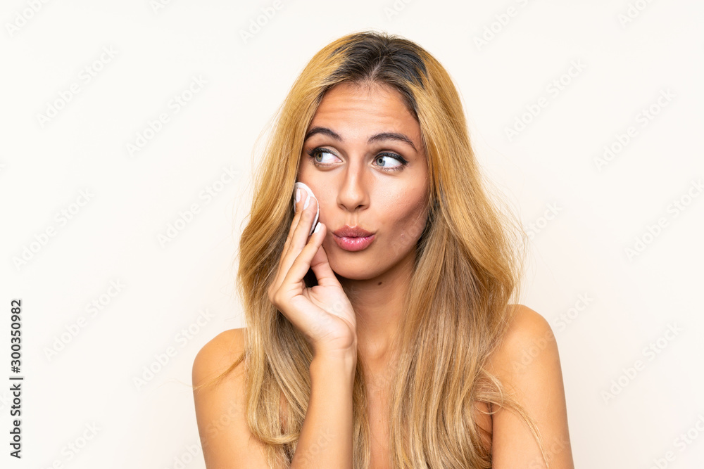 Young blonde woman removing makeup from her face with cotton pad Young blonde woman removing makeup from her face with cotton pad
