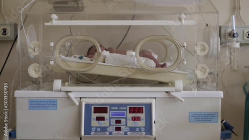Premature newborn baby in diapers sleeping during treatment in incubator apparatus at hospital intensive care unit, interior scene.