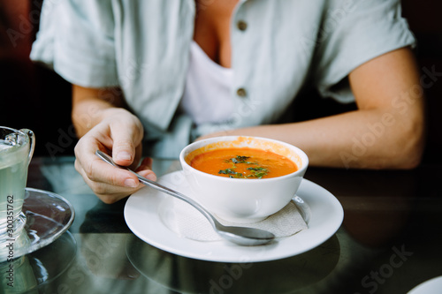 Closeup shot of a woman holding a spoon to eat her tomato soup in a cafe
