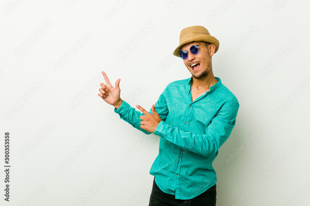 Young hispanic man wearing a summer clothes pointing with forefingers to a copy space, expressing excitement and desire.
