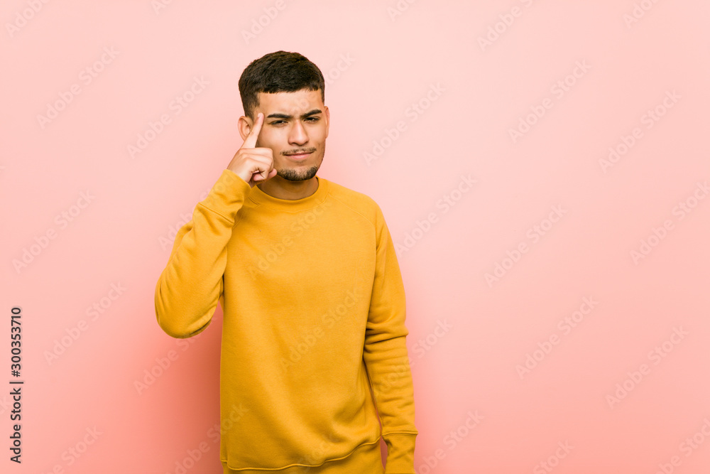 Young hispanic man pointing temple with finger, thinking, focused on a task. Young hispanic man pointing temple with finger, thinking, focused on a task.