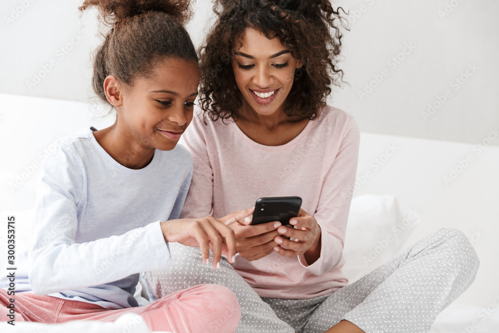 Image of american woman and her little daughter using cellphone at home Image of american woman and her little daughter using cellphone at home