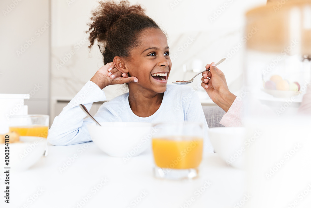 Image of american woman feeding her daughter while having breakfast Image of american woman feeding her daughter while having breakfast