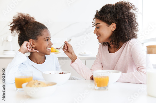 Image of american woman feeding her daughter while having breakfast